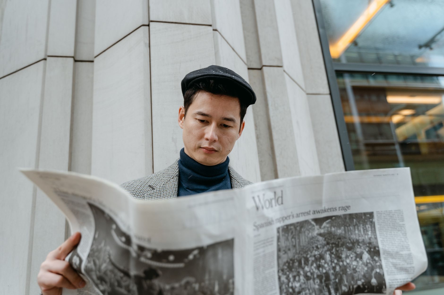 A young man in a flat cap and turtleneck reads a newspaper outdoors. — How to Choose the Right Medicare Advantage Plan in 202