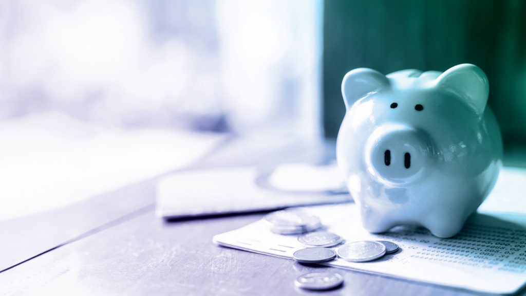 A blue piggy bank surrounded by coins and a financial statement on a wooden table.